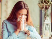 Flu. Young woman got nose allergy, flu sneezing nose sitting at the table in a trendy cafe coffee shop with a cup of hot beverage beside
